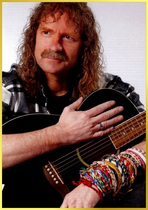 Wolfgang Petry Double Portrait mit bunten Freundschaftsbändern am Handgelenk und Gitarre im Arm.